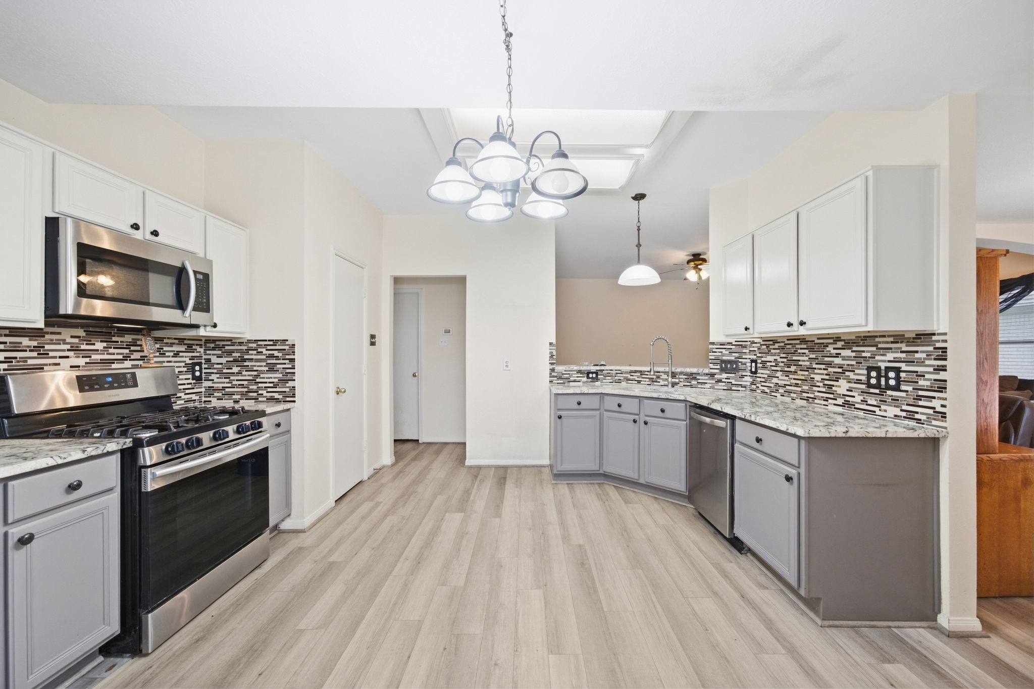 6911 River Road Richmond, TX 77469 - Photo 17 of 36 Centering the kitchen workspace, two-tone cabinetry surrounds a stainless steel gas range, built-in microwave, and undermount corner sink. Granite countertops, mosaic tile, and durable wood-look flooring establish an efficient layout tailored for everyday utility and solid investment potential.