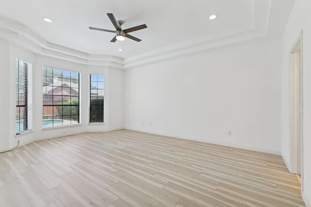 an empty room with wooden floor fan and windows
