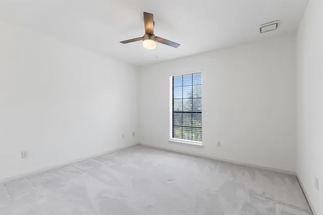 an empty room with chandelier fan and windows