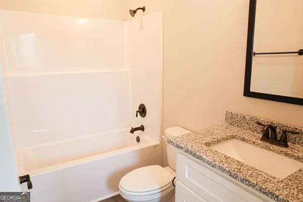 a bathroom with a granite countertop bathtub sink vanity mirror and toilet