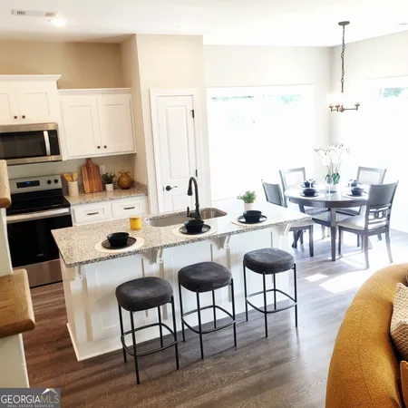 a kitchen with stainless steel appliances kitchen island granite countertop a dining table chairs and a refrigerator