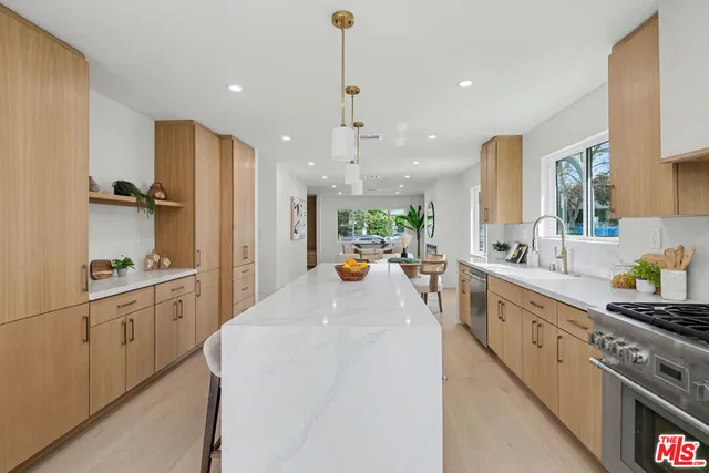 a large kitchen with stainless steel appliances a large counter top a stove a chimney a sink and a refrigerator