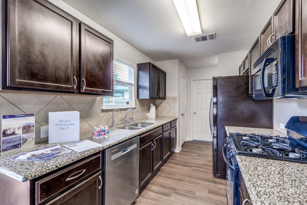 13708 Sierra Wind Lane Elgin, TX 78621 - Photo 9 of 19 Kitchen with black appliances, light wood-style floors, light stone counters, dark brown cabinets, and a textured ceiling