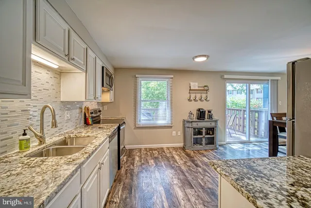 a kitchen with granite countertop a stove top oven a sink dishwasher a dining table and chairs with wooden floor