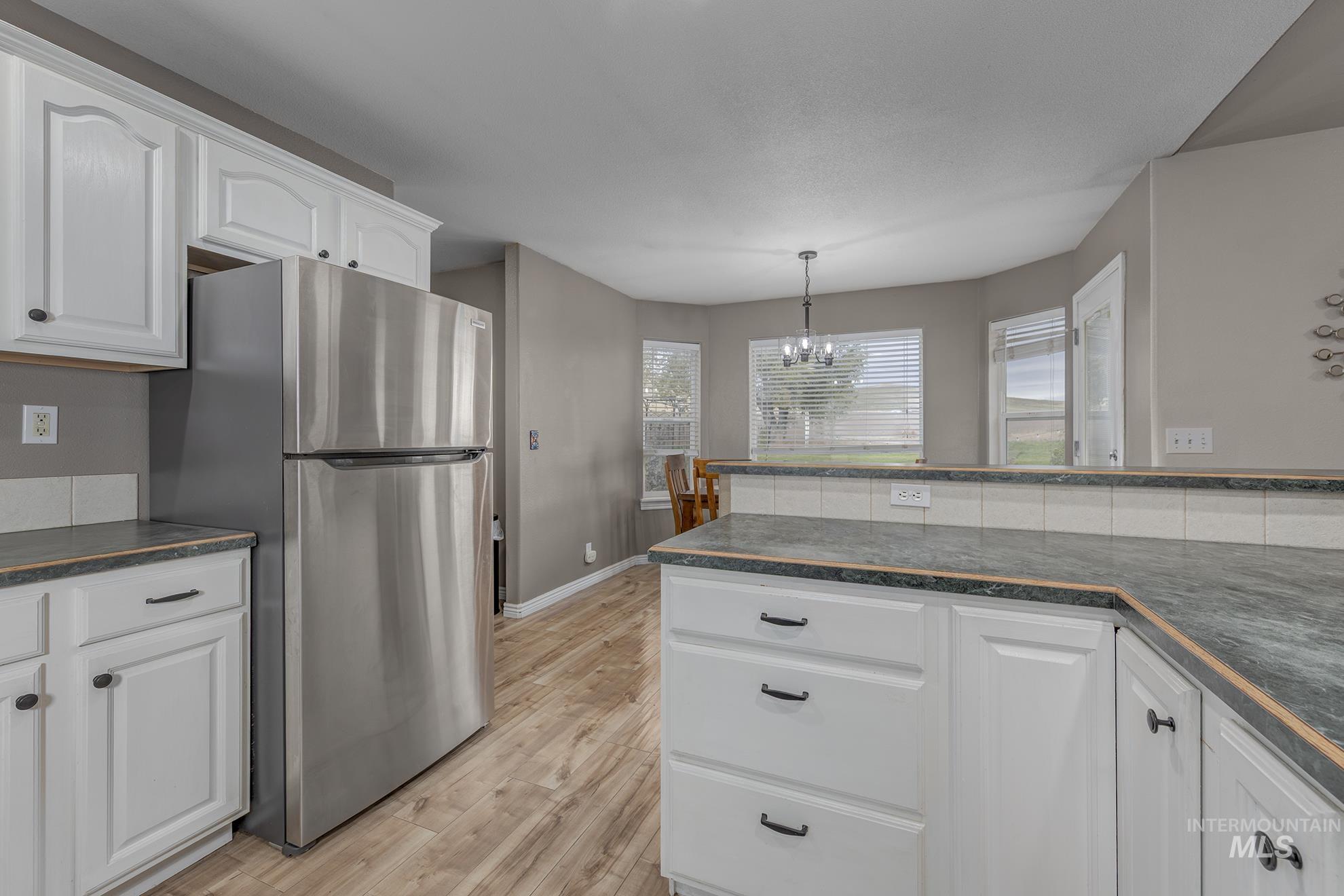 890 Jenkins Creek Road Weiser, ID 83672 - Photo 12 of 45 Kitchen with white cabinets, freestanding refrigerator, light wood-style flooring, and a chandelier