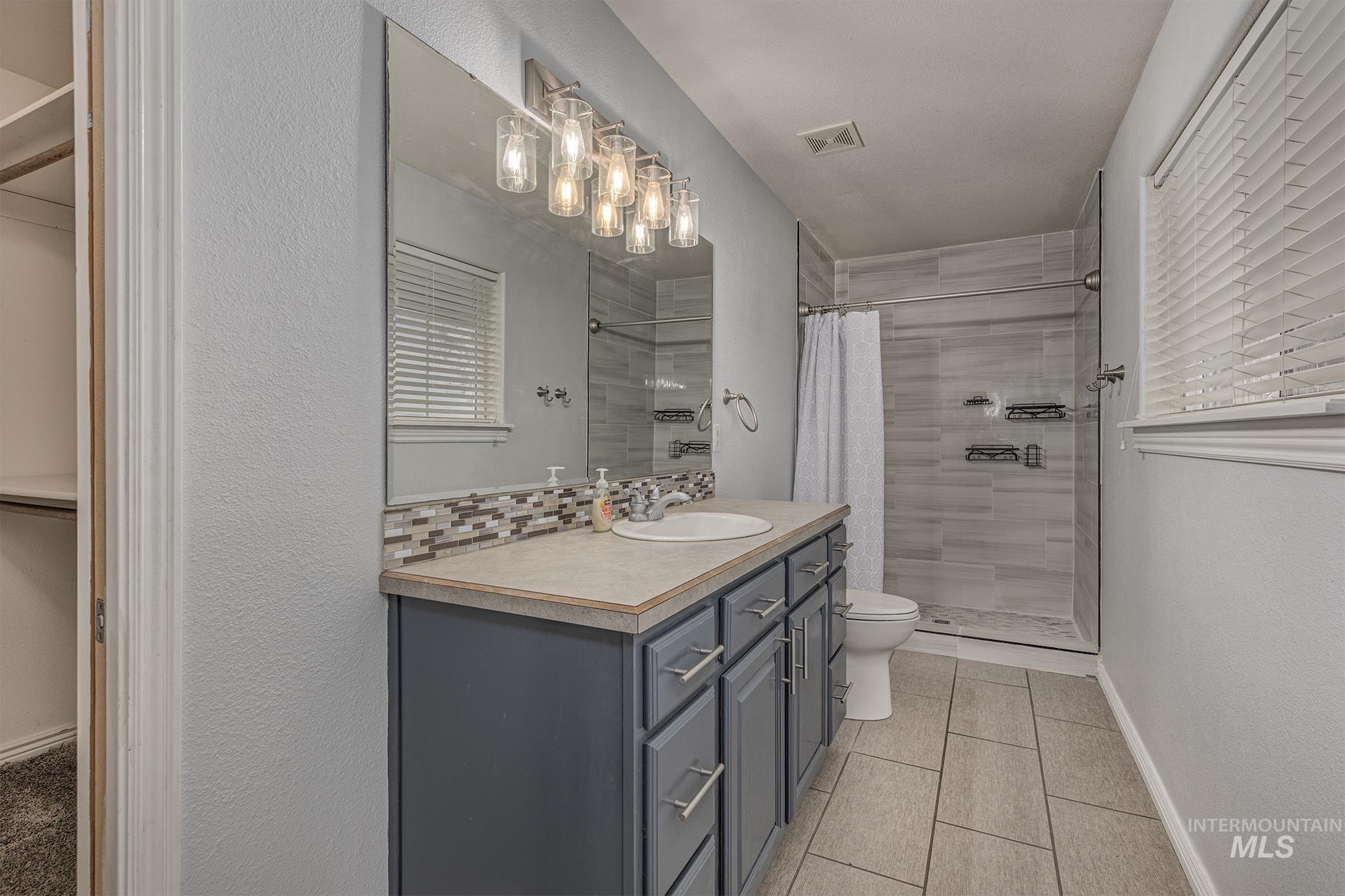 890 Jenkins Creek Road Weiser, ID 83672 - Photo 17 of 45 Full bathroom featuring a spacious closet, vanity, light tile patterned floors, a shower stall, and tasteful backsplash