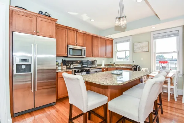 a kitchen with granite countertop a refrigerator a sink a stove and chairs with wooden floor