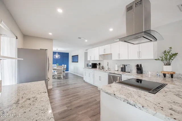 a large kitchen with stainless steel appliances granite countertop a stove top oven a refrigerator and white cabinets with wooden floor