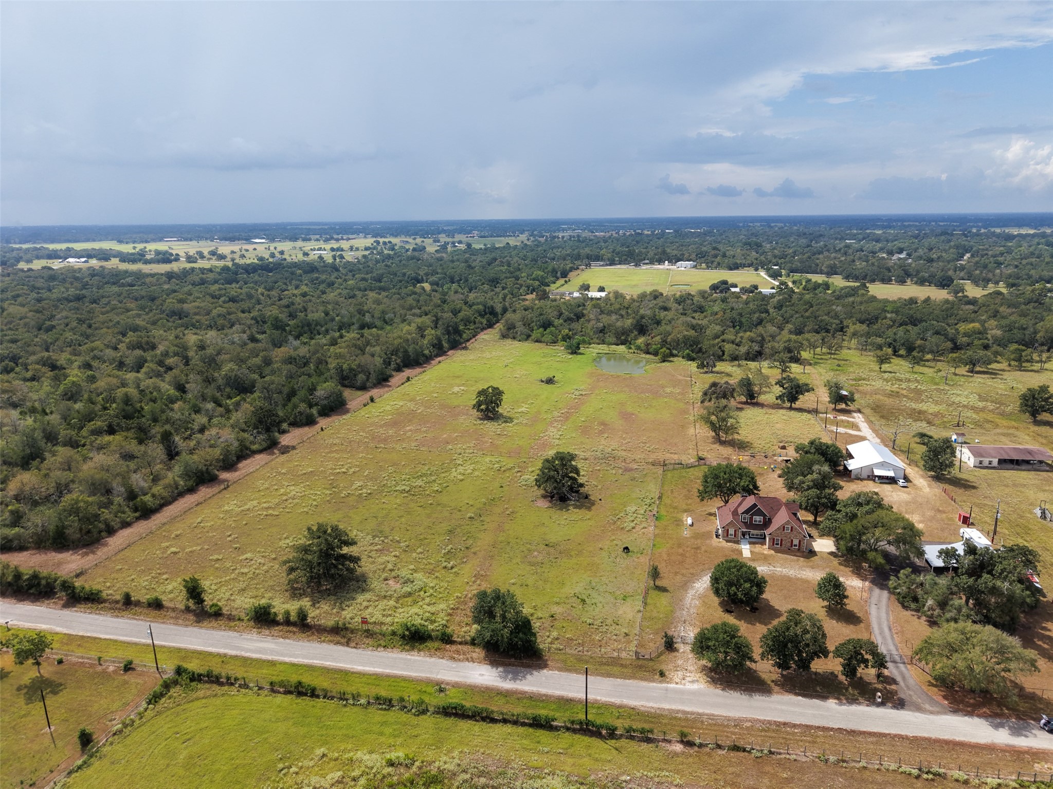 38021 Wiggins Road Hempstead, TX 77445 - Photo 2 of 19 Angled aerial perspective highlights the tract’s open acreage, road access, and attractive mix of pasture, pond and mature trees.