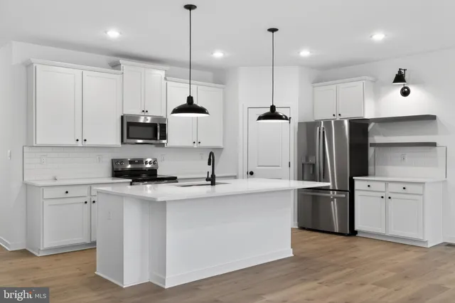 a kitchen with stainless steel appliances kitchen island granite countertop a sink a stove a refrigerator and white cabinets with wooden floor