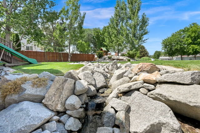 13658 South Fort Street Draper, UT 84020 - Photo 63 of 87 Expansive backyard featuring a rock-lined water feature, lush green lawn, mature trees, and a privacy fence