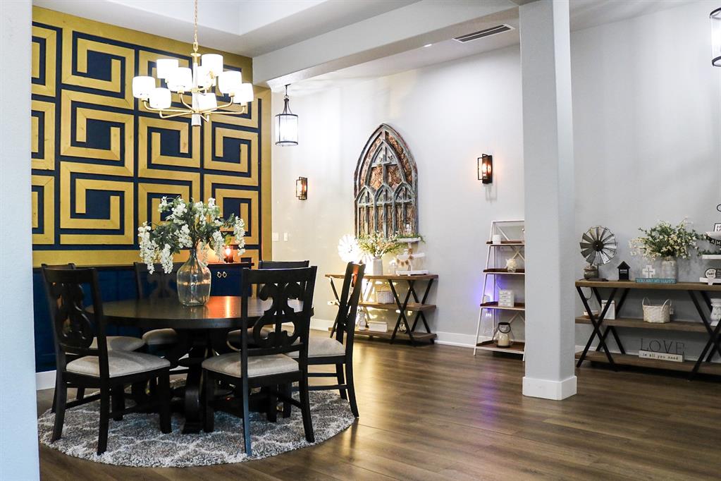 997 Ovilla Road Waxahachie, TX 75167 - Photo 11 of 32 Dining area featuring a prominent accent wall with a geometric pattern, gold-tone chandelier, wood-finish flooring, and light gray wall paint