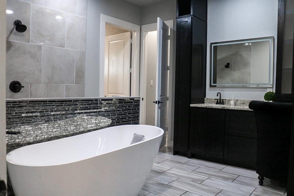 997 Ovilla Road Waxahachie, TX 75167 - Photo 12 of 32 Contemporary bathroom featuring a freestanding soaking tub, large format tile shower surround, and a dark wood-finish vanity with a light-colored countertop