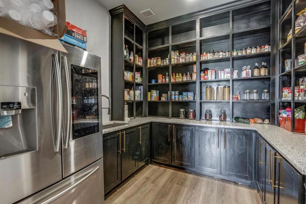 997 Ovilla Road Waxahachie, TX 75167 - Photo 27 of 32 Expansive pantry featuring extensive dark wood cabinetry and shelving, light-toned countertops, a built-in stainless steel refrigerator, and wood-finish flooring