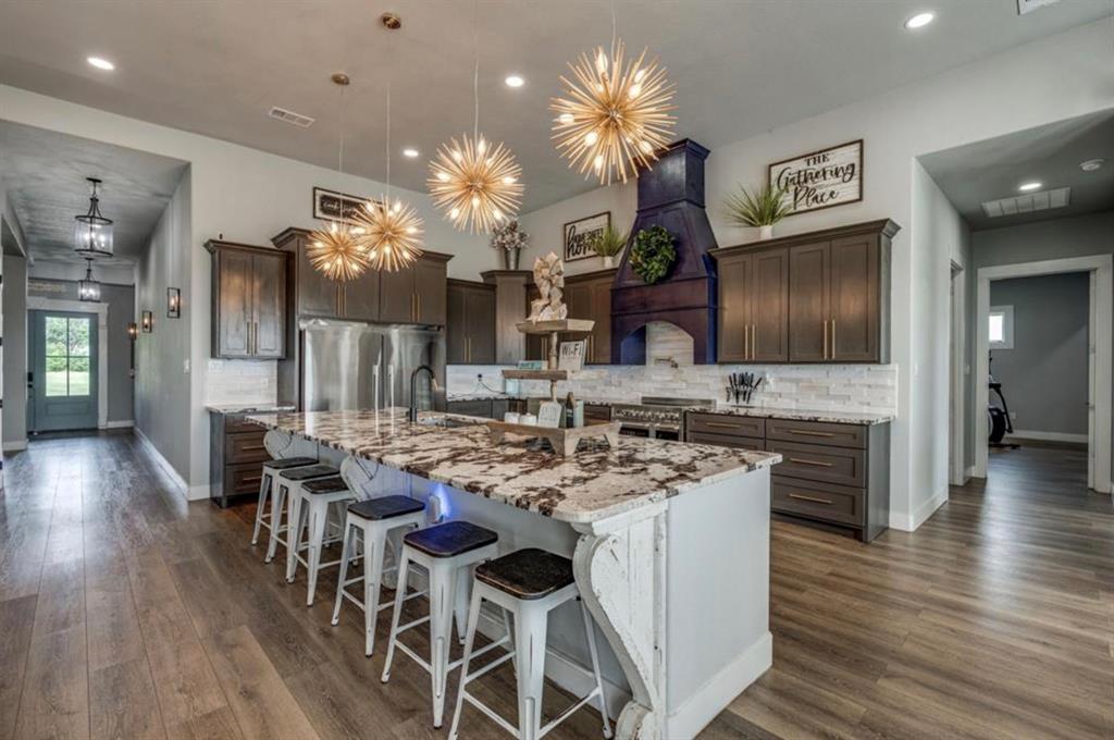 997 Ovilla Road Waxahachie, TX 75167 - Photo 29 of 32 Gourmet kitchen featuring a large island with a stone countertop, dark wood-finish cabinetry, stainless steel appliances, a tile backsplash, and decorative pendant lighting