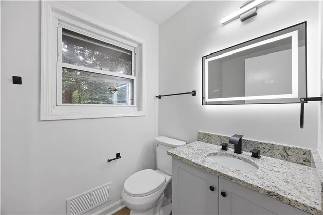 a bathroom with a granite countertop toilet a sink and mirror