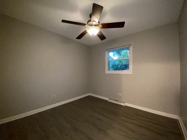 a view of an empty room with wooden floor and a ceiling fan