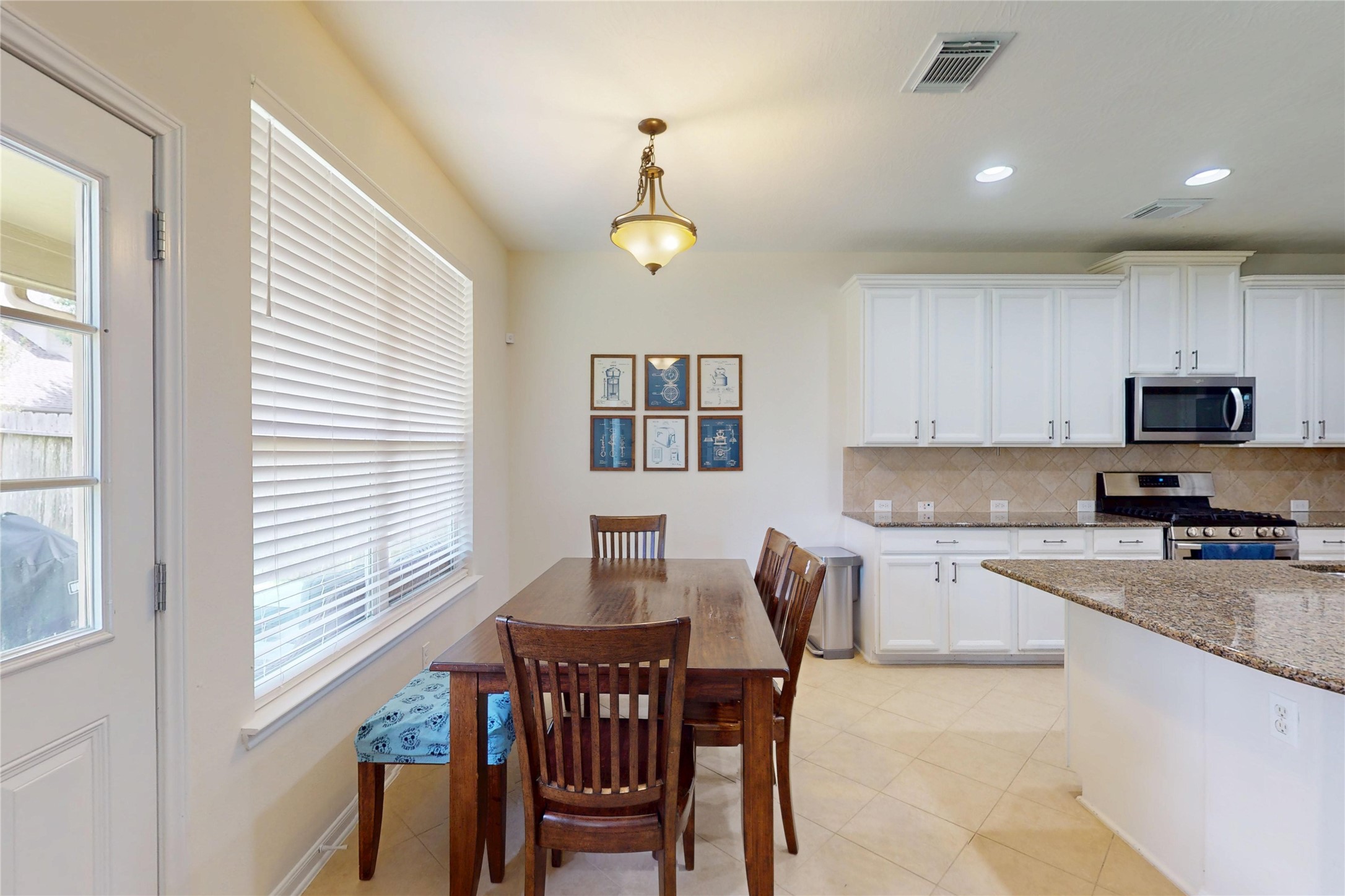 17402 Rainer Valley Lane Humble, TX 77346 - Photo 14 of 33 Bright kitchen and dining area with natural light, featuring tile flooring and white cabinetry. Includes a dining table, stainless steel appliances, and a granite countertop. Ideal for family meals and entertaining.