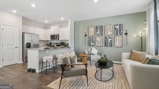a living room with white couches and kitchen view with wooden floor