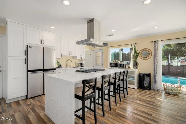 a kitchen with stainless steel appliances a refrigerator a stove a dining table and chairs with wooden floor