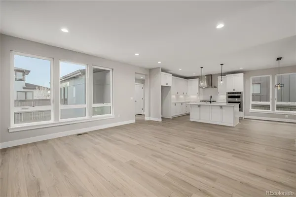 a view of an empty room with wooden floor and kitchen