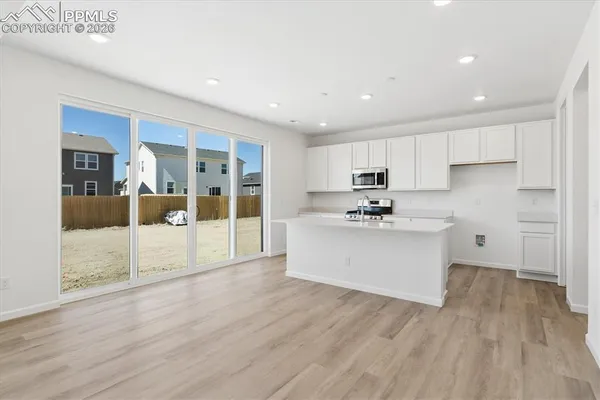 a view of kitchen with granite countertop refrigerator oven sink and white cabinets with wooden floor
