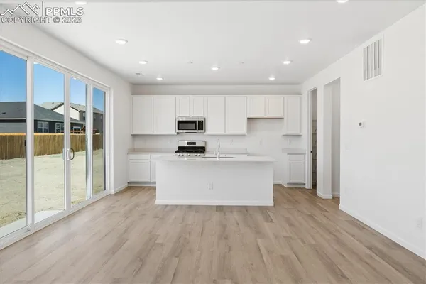 a view of kitchen with granite countertop refrigerator oven sink and white cabinets with wooden floor