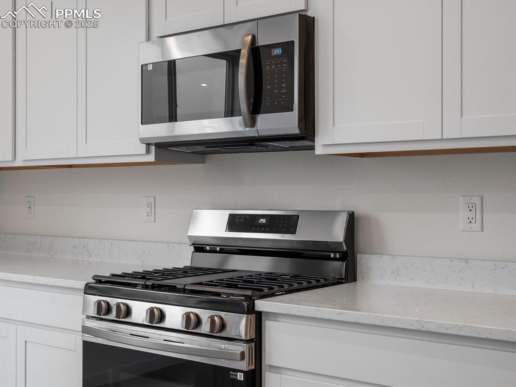 10768 Lewanee Point Colorado Springs, CO 80908 - Photo 12 of 32 Kitchen with appliances with stainless steel finishes, white cabinets, and light stone countertops