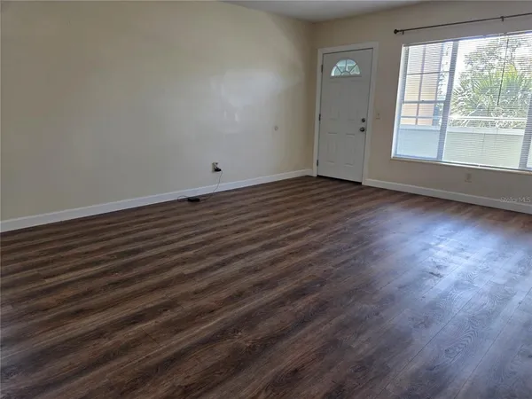 a view of an empty room with wooden floor and a window