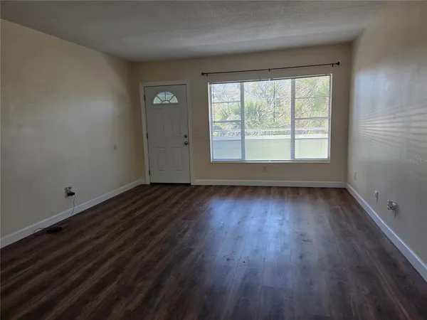 a view of an empty room with wooden floor and a window