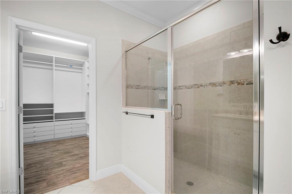 6934 Avalon Circle, Unit 405 Naples, FL 34112 - Photo 11 of 16 Bathroom featuring a stall shower, a walk in closet, light tile patterned floors, and crown molding