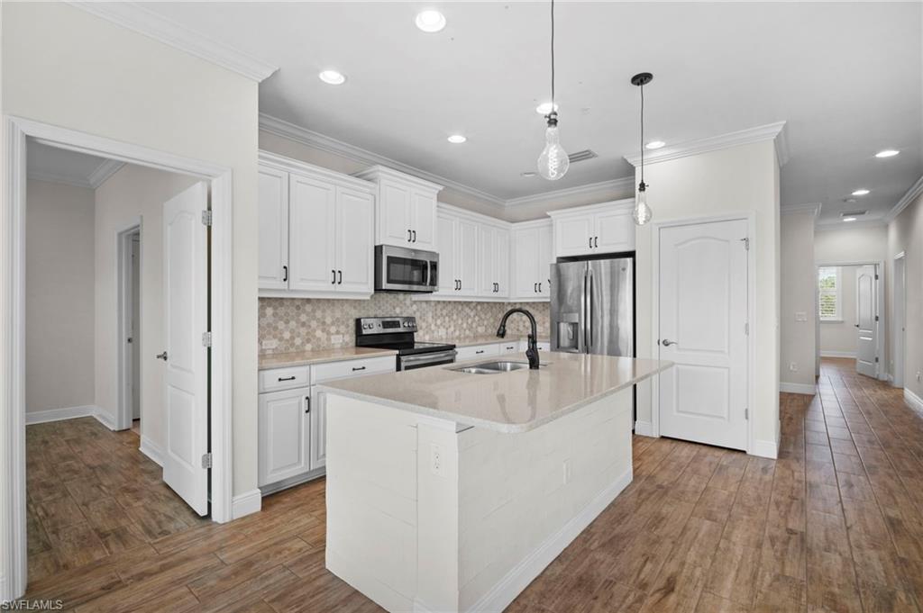 6934 Avalon Circle, Unit 405 Naples, FL 34112 - Photo 3 of 16 Kitchen with stainless steel appliances, white cabinetry, an island with sink, decorative light fixtures, and crown molding