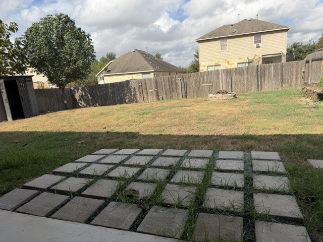571 Dragon Ridge Road Buda, TX 78610 - Photo 15 of 16 An expansive fenced backyard features a paved patio area and a stone fire pit.