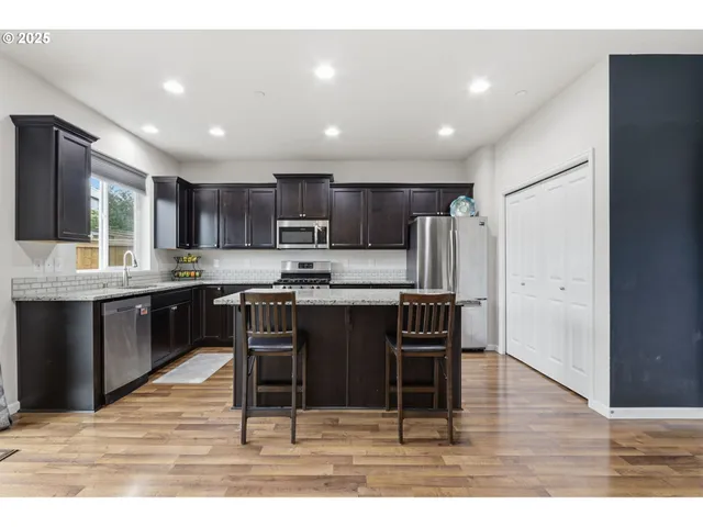 a kitchen with kitchen island granite countertop wooden floors appliances and cabinets