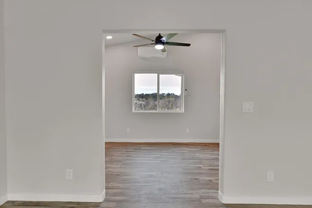 an empty room with wooden floor fan and windows