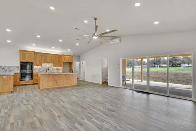 a view of an empty room with wooden floor and a kitchen