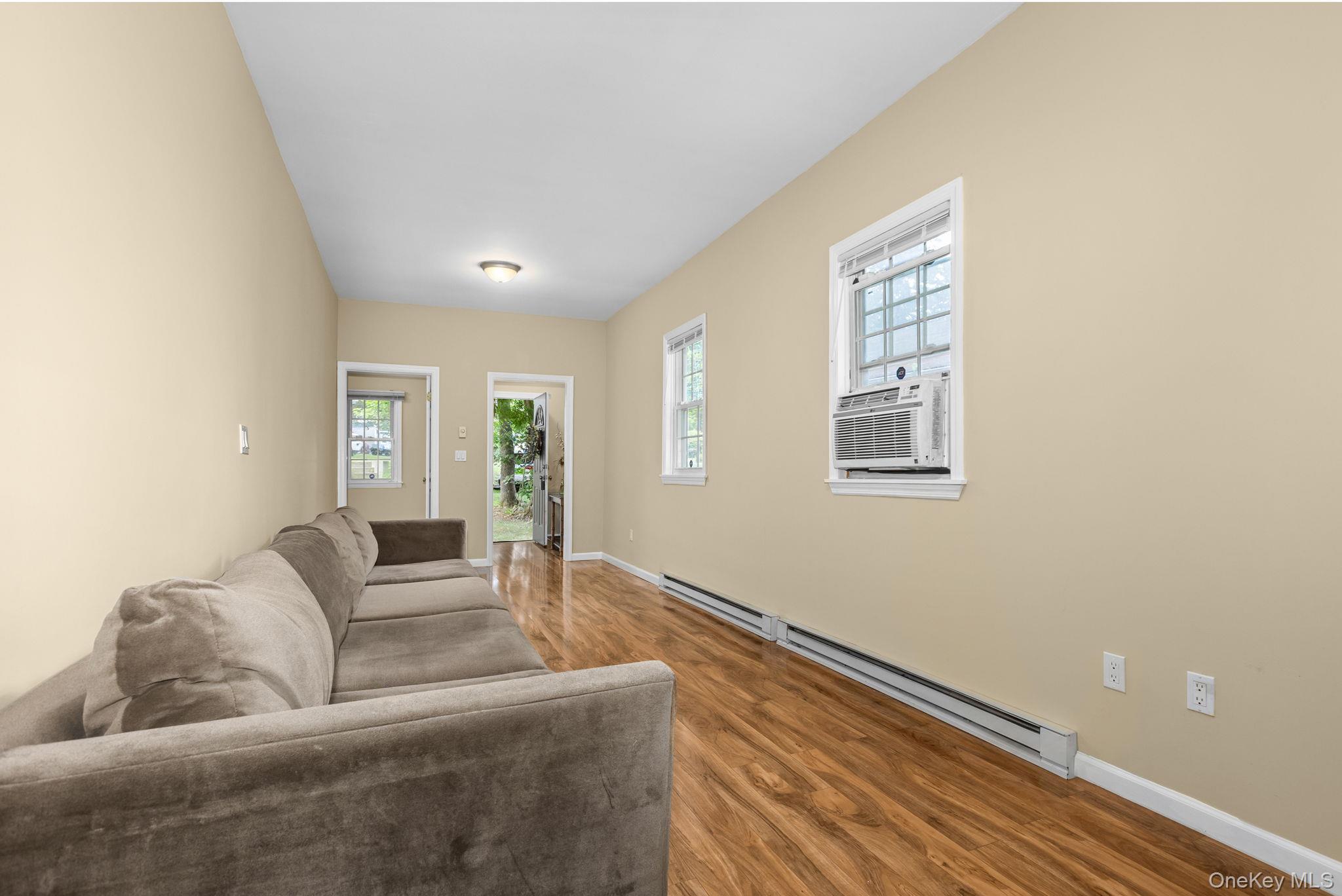 10 Batavia Road Patterson, NY 12563 - Photo 7 of 42 Spacious room featuring wood-finish flooring, two windows with white trim, a window-mounted air conditioning unit, and baseboard heating