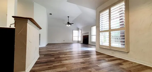 an empty room with wooden floor chandelier fan and windows