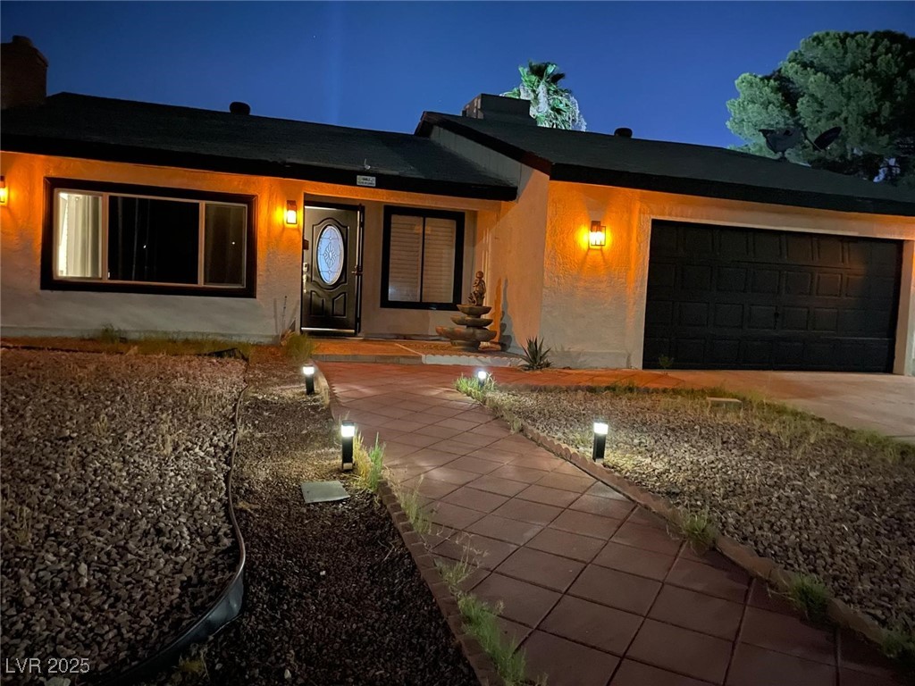 View of front of house with a garage, a chimney, driveway, and stucco siding