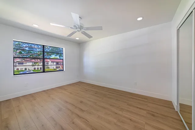 an empty room with wooden floor ceiling fan and windows