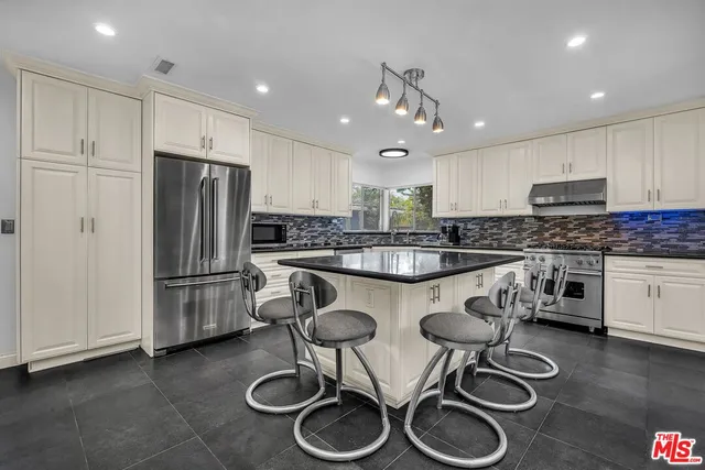 a kitchen with stainless steel appliances granite countertop a sink a stove a refrigerator and white cabinets with wooden floor