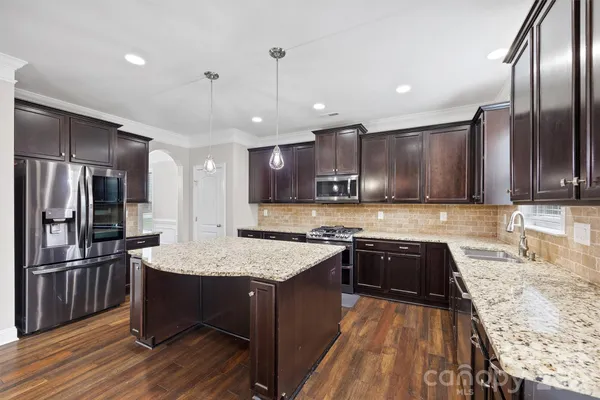 a large kitchen with granite countertop a large counter top stainless steel appliances and wooden floor