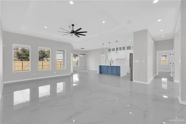 a view of an empty room with a kitchen and chandelier fan