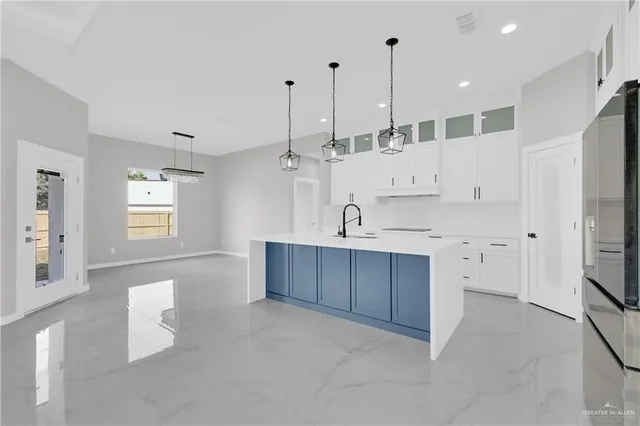 a large kitchen with kitchen island a stove a sink a refrigerator and white cabinets with wooden floor