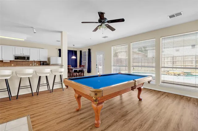 a room with wooden floors pool table and windows