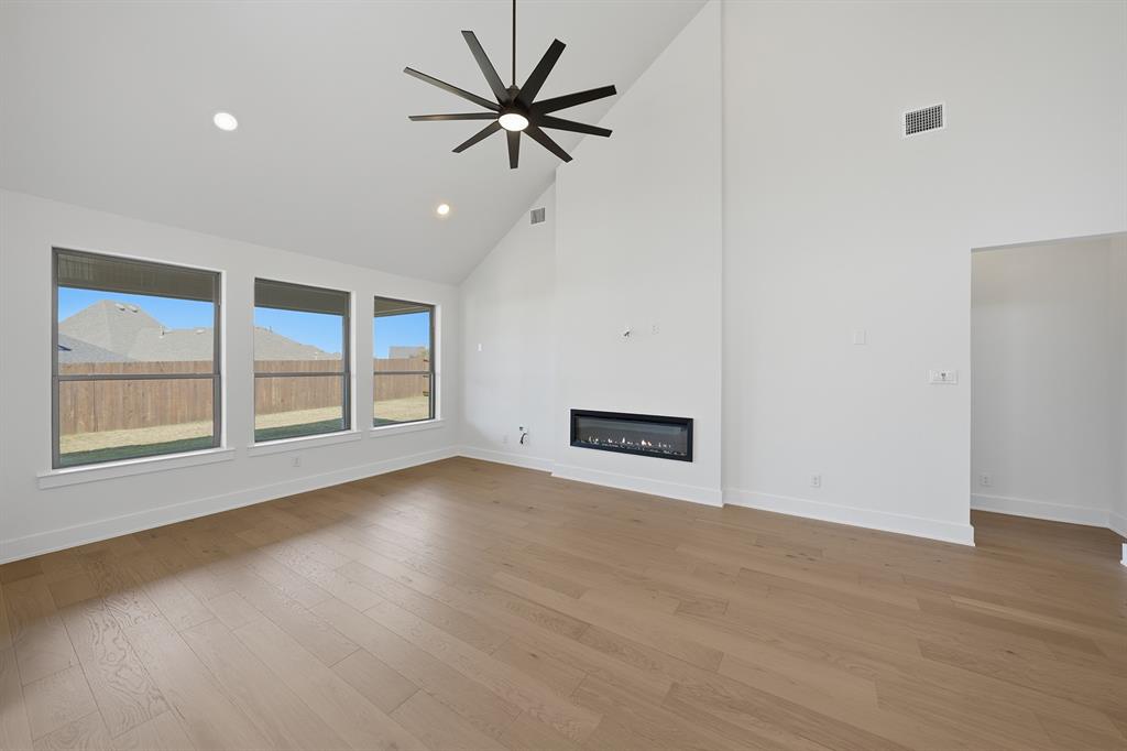 6028 Foxwheel Way Fort Worth, TX 76123 - Photo 11 of 37 Unfurnished living room with high vaulted ceiling, a glass covered fireplace, light wood-style floors, a ceiling fan, and recessed lighting