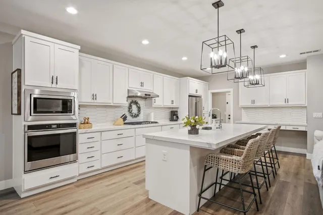 a kitchen with stainless steel appliances kitchen island granite countertop a stove a sink a dining table and chairs with wooden floor