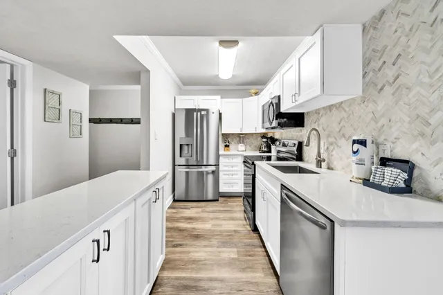 a kitchen with granite countertop a refrigerator a sink dishwasher a stove and white cabinets with wooden floor