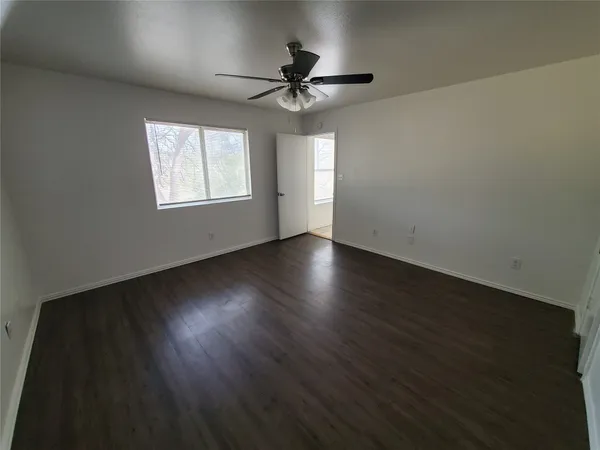 an empty room with wooden floor chandelier fan and windows