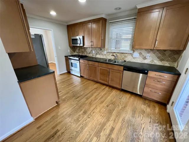 a kitchen with granite countertop a sink a stove top oven a refrigerator and wooden floors